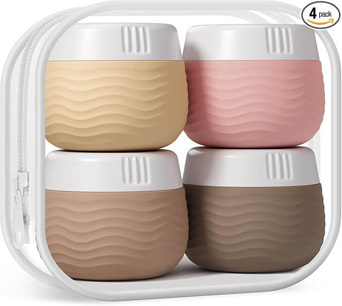 Four small, round containers in beige, pink, light brown, and dark brown with white lids are nestled in a transparent zippered case. This sleek set is one of the best travel accessories for keeping your essentials organized on the go.