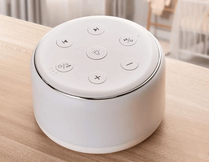 A round white sound machine, one of the best travel accessories, with control buttons is placed on a wooden surface.