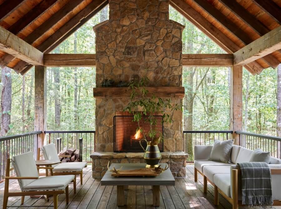 23 New Boutique Hotels in the South - 7 A cozy outdoor room in the style of new boutique hotels features a stone fireplace, surrounded by sofas and chairs on a wooden deck, overlooking a wooded area.