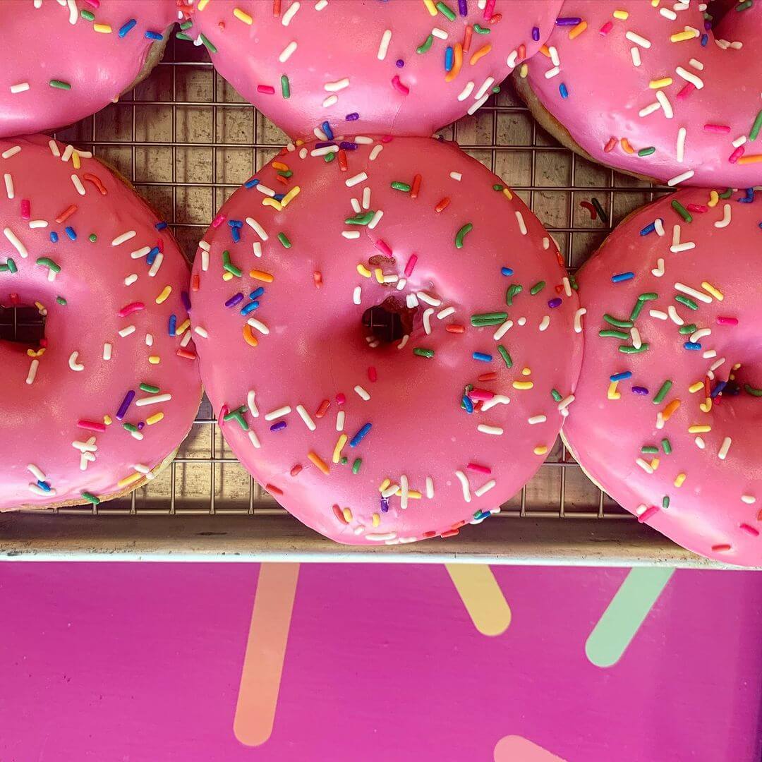A tray of pink donuts with sprinkles on top.