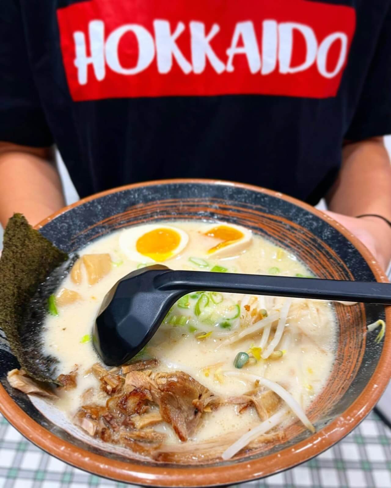 A person holding a bowl of ramen with an egg in it.
