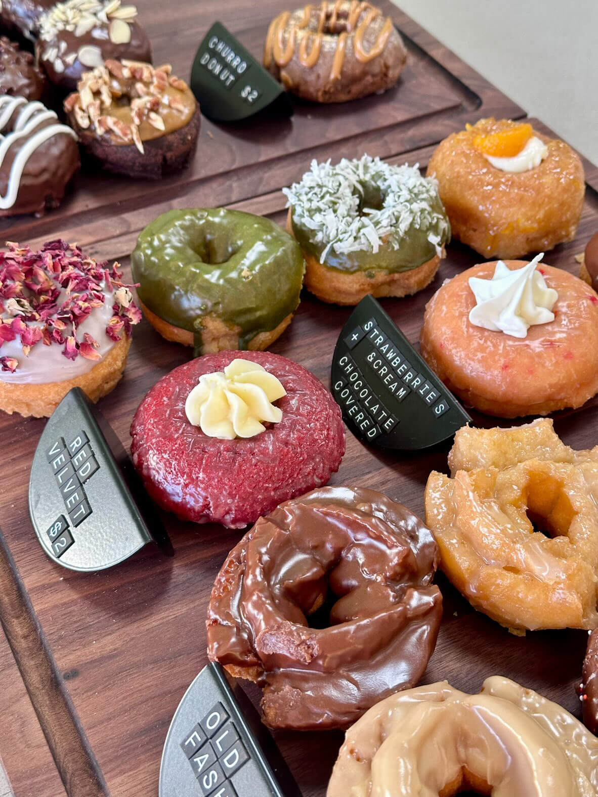 An assortment of gourmet donuts with various toppings from new Louisville restaurants displayed on a wooden surface.