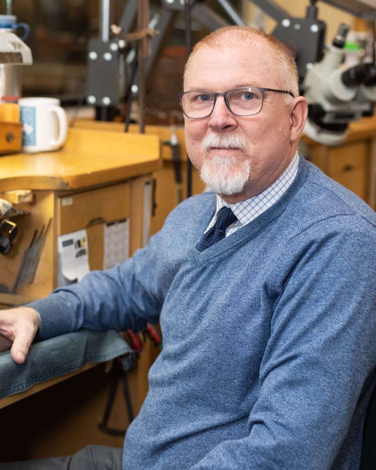 Man in blue sweater sitting in jewelry workshop