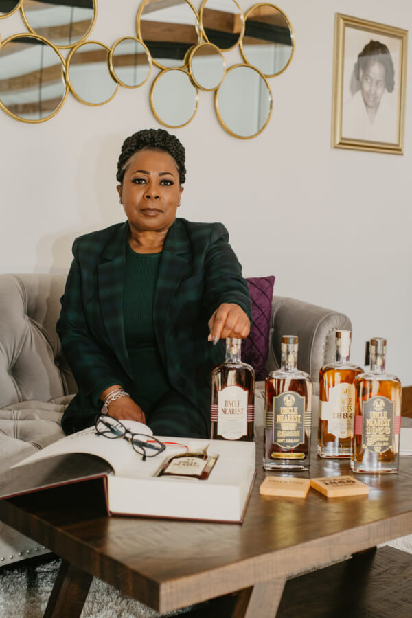 Woman sitting on a couch in front of a coffee table with various whiskey bottles.