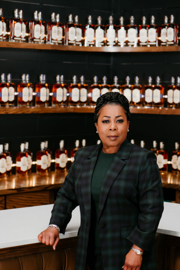 Woman in plaid jacket, in front of whiskey bottles