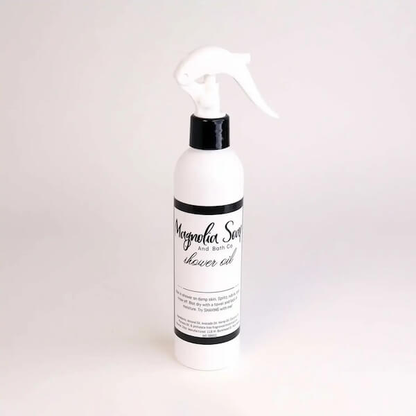White spray bottle labeled "Magnolia Soap and Bath Co. shower oil" with a black nozzle, featured as a Southern FINDS pick for February, on a plain background.