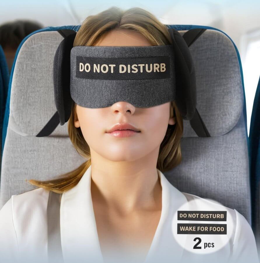 A person on a plane sports one of the best travel accessories—a black eye mask emblazoned with "DO NOT DISTURB." Two pieces are featured in the image, highlighting this essential item for undisturbed rest mid-flight.