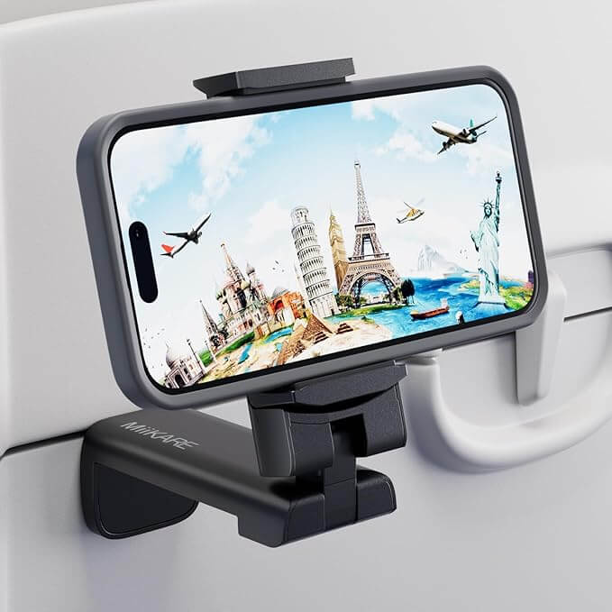 A phone, considered one of the best travel accessories, is mounted on an airplane tray table holder. It displays an illustration of global landmarks like the Eiffel Tower and Statue of Liberty, with planes flying in the background.