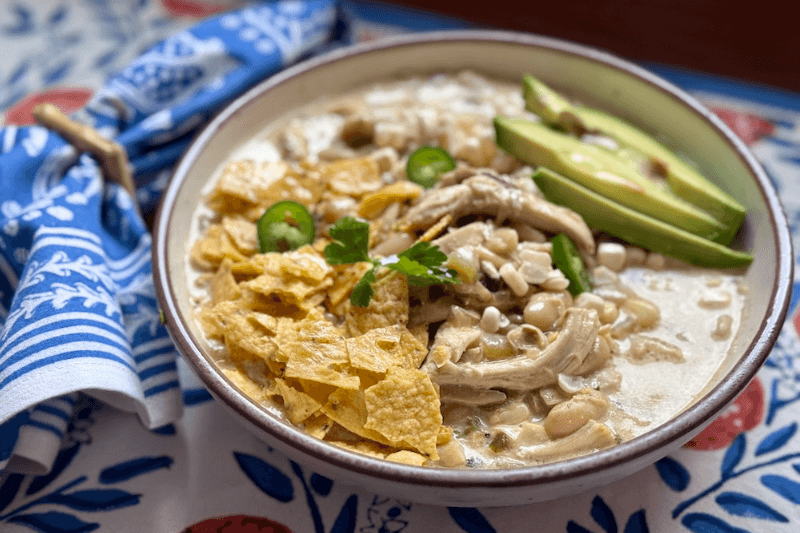 A bowl of white chicken chili soup with tortilla chips and avocado.