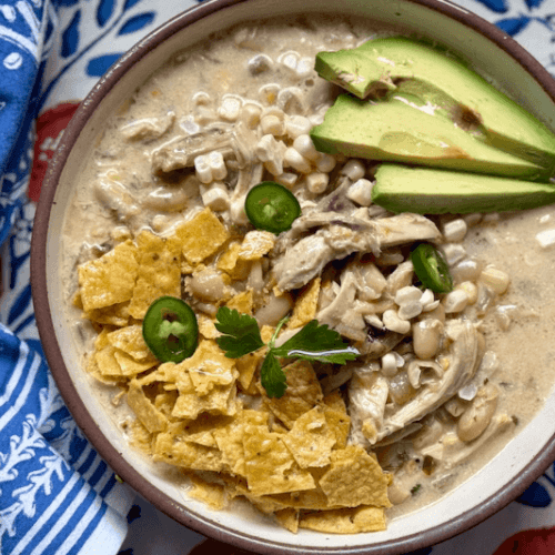 A bowl of soup with avocado and tortilla chips.
