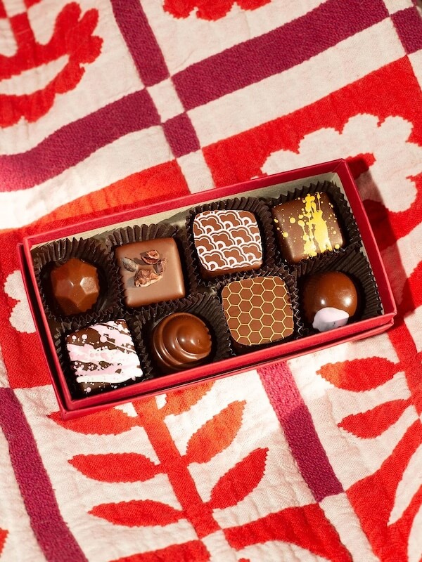 A red box of eight assorted chocolates, featuring various designs, sits elegantly on a red and white patterned cloth, capturing the charm of Southern FINDS in February.