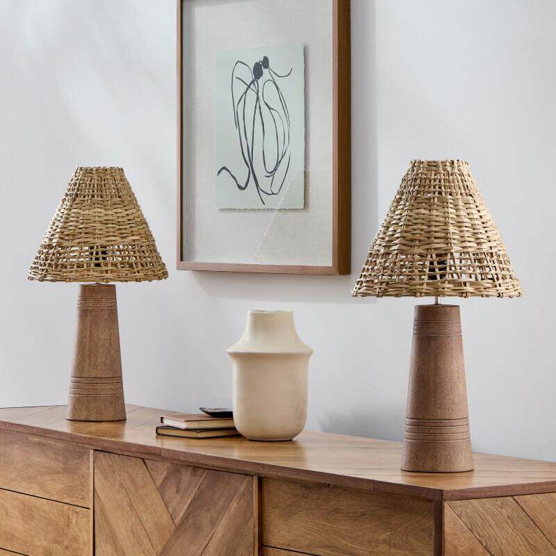 Two exquisite wicker lamps and a white vase elegantly positioned on a wooden sideboard, complemented by a framed abstract artwork above.