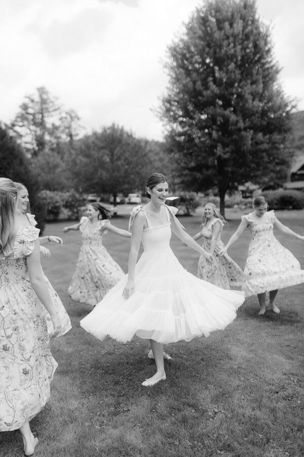 A North Carolina Wedding Dressed in Blues, Bows, and Bojangles - 10 A black and white photo of bridesmaids dancing in the grass.