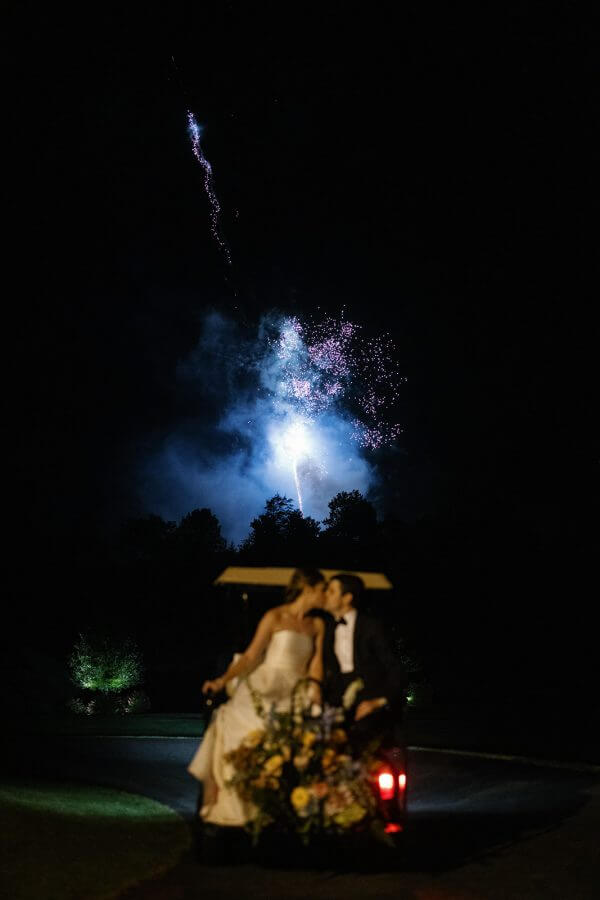 A North Carolina Wedding Dressed in Blues, Bows, and Bojangles - 24 A bride and groom in a golf cart with fireworks in the background.