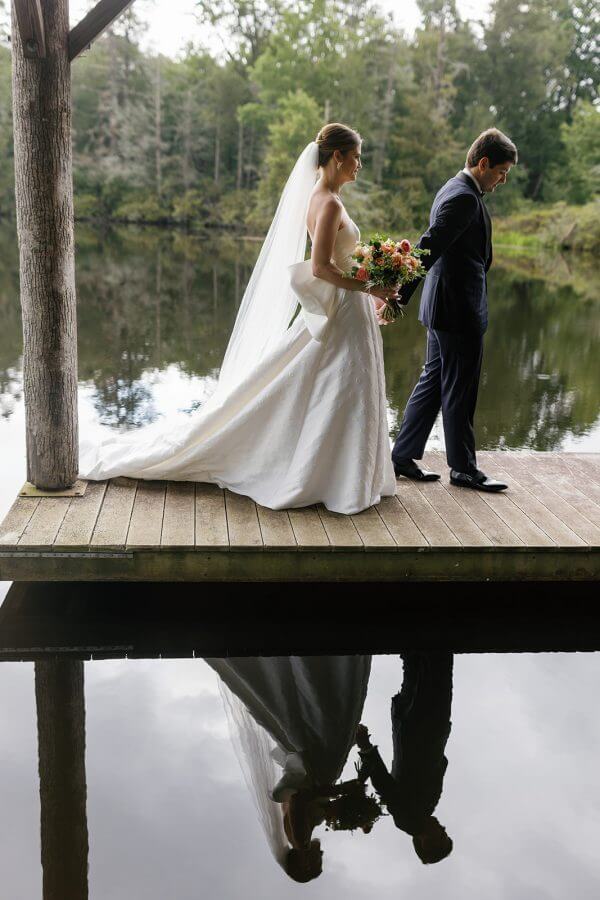 A North Carolina Wedding Dressed in Blues, Bows, and Bojangles - 4 A bride and groom standing on a dock next to a lake at their Linville wedding.