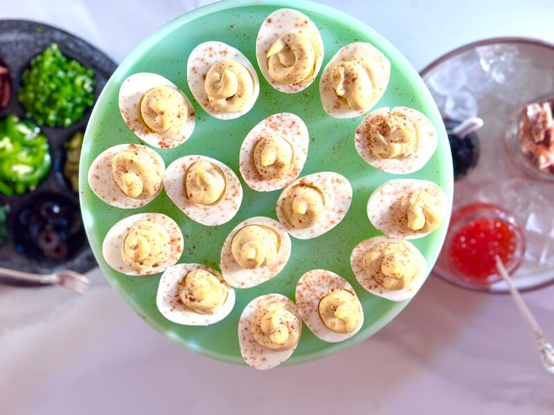 A deviled egg bar setup, featuring a plate of deviled eggs garnished with paprika, surrounded by ingredients.