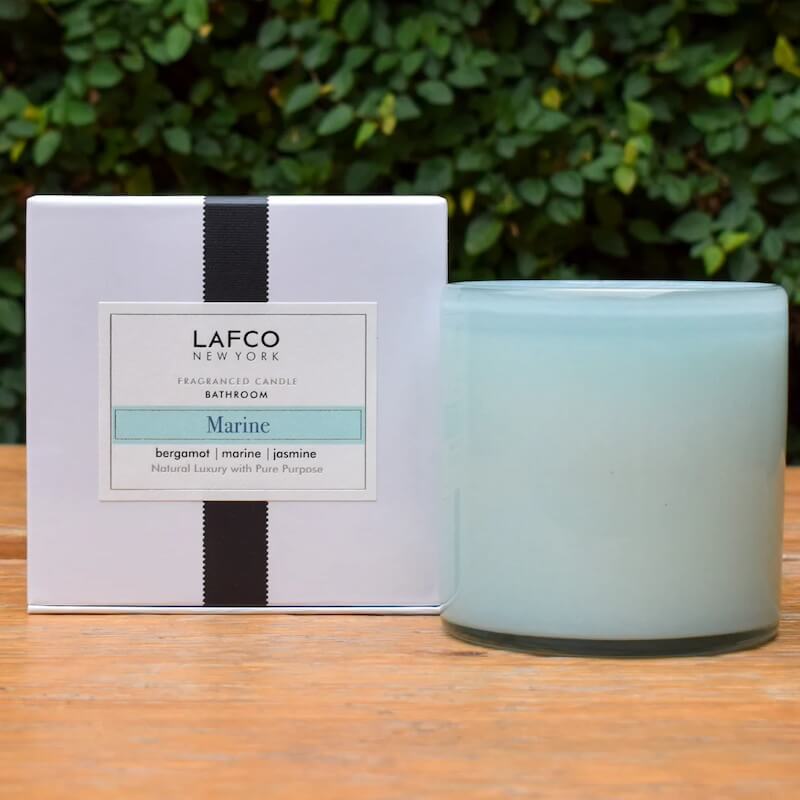 On a wooden surface, the "Marine" candle by Lafco New York exudes scents of bergamot, marine, and jasmine.