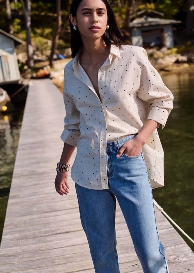 Person wearing a polka dot shirt and jeans standing on a wooden dock during their March finds, with cabins and trees in the background.