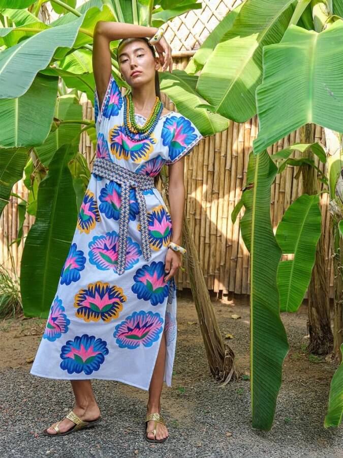 Person posing in a vibrant floral dress and sandals, showcasing their latest March finds while standing among banana plants with a bamboo fence in the background.