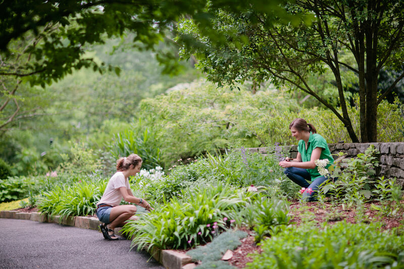 Two women kneeling on a path in a garden.