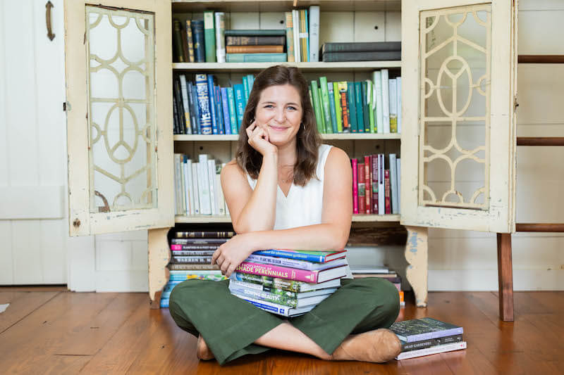 A woman sitting on the floor with a stack of books in front of a bookcase.