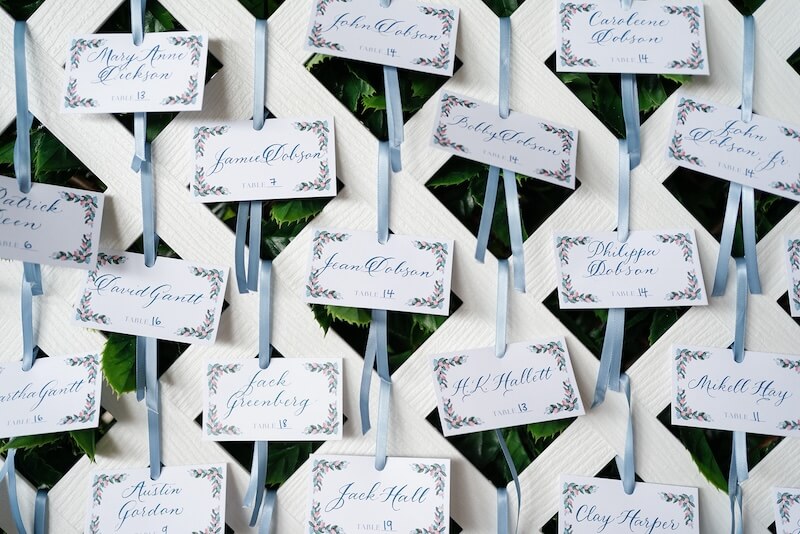 A North Carolina Wedding Dressed in Blues, Bows, and Bojangles - 19 An array of seating cards with names and table numbers, attached to a decorative board with ribbons for a North Carolina wedding.