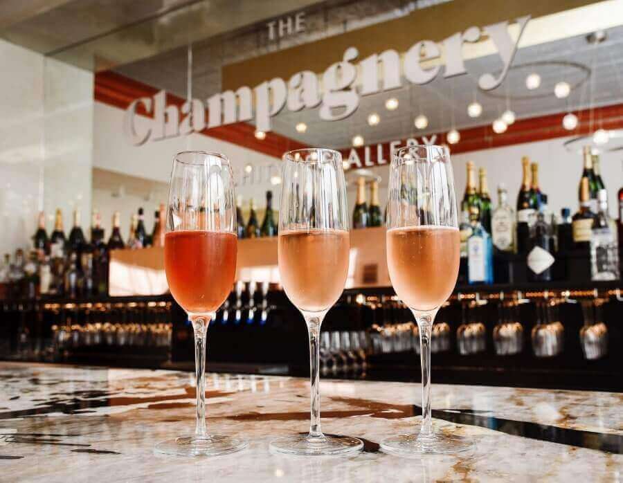 Three glasses of rosé champagne on a bar counter with a sign reading 