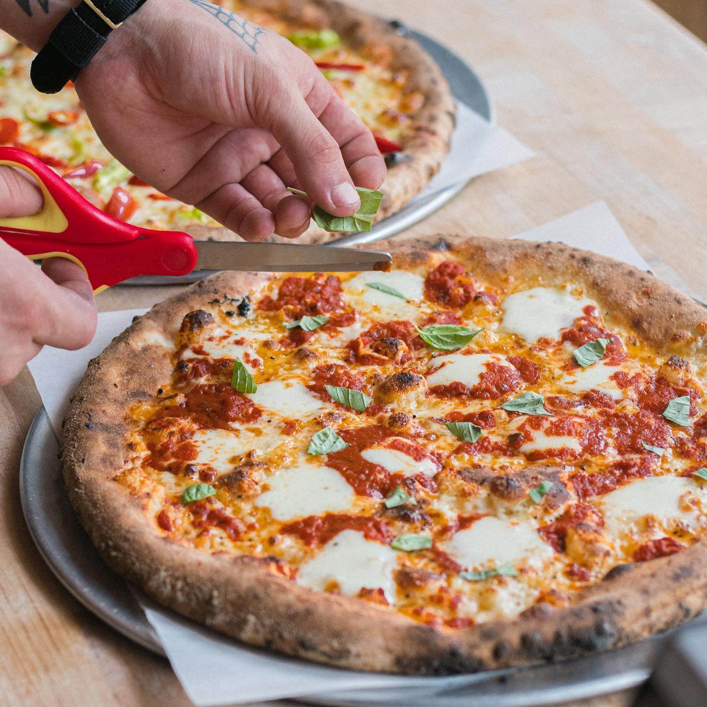 A person slicing a freshly baked pizza topped with cheese and basil.