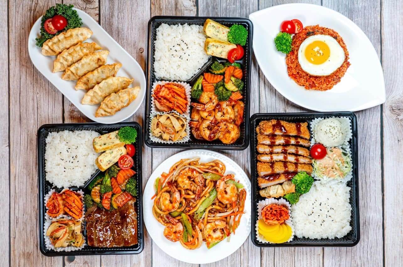 Assorted asian cuisine bento boxes and side dishes displayed on a wooden table.