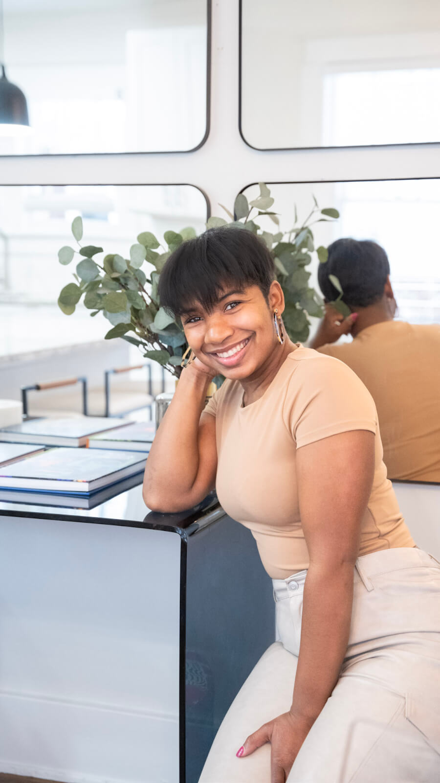 A smiling person sitting at a table with their chin resting on their hand.