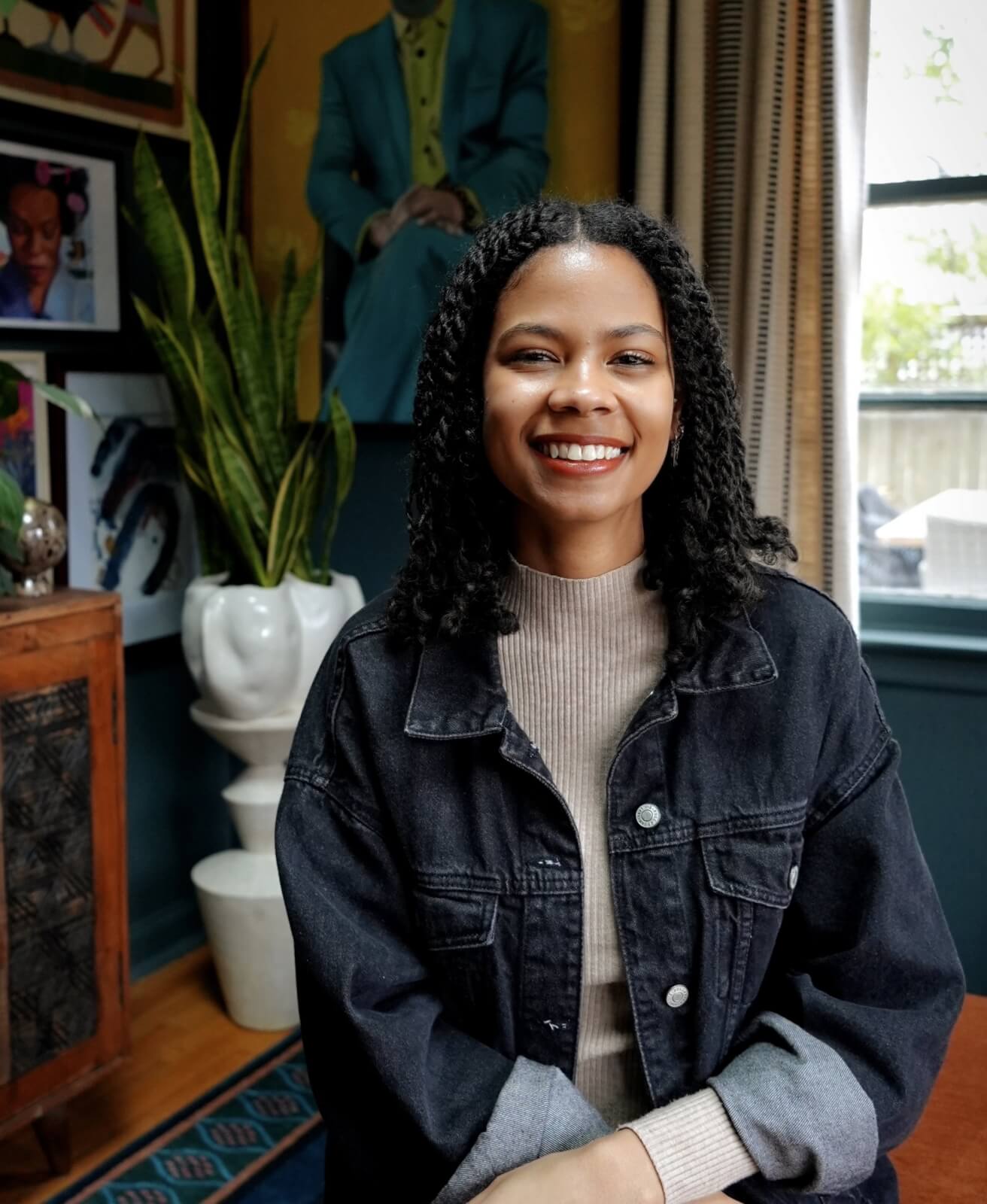 Young woman smiling in a room with artwork and plants.