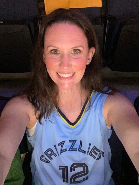 A smiling woman in a grizzlies jersey taking a selfie at a basketball arena.
