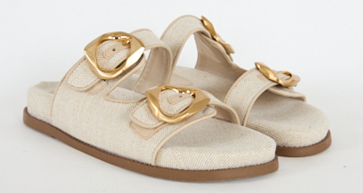 Beige sandals with two wide straps, each featuring a large gold buckle, and flat brown soles, reminiscent of the effortless style found at Nashville's FINDS in March.