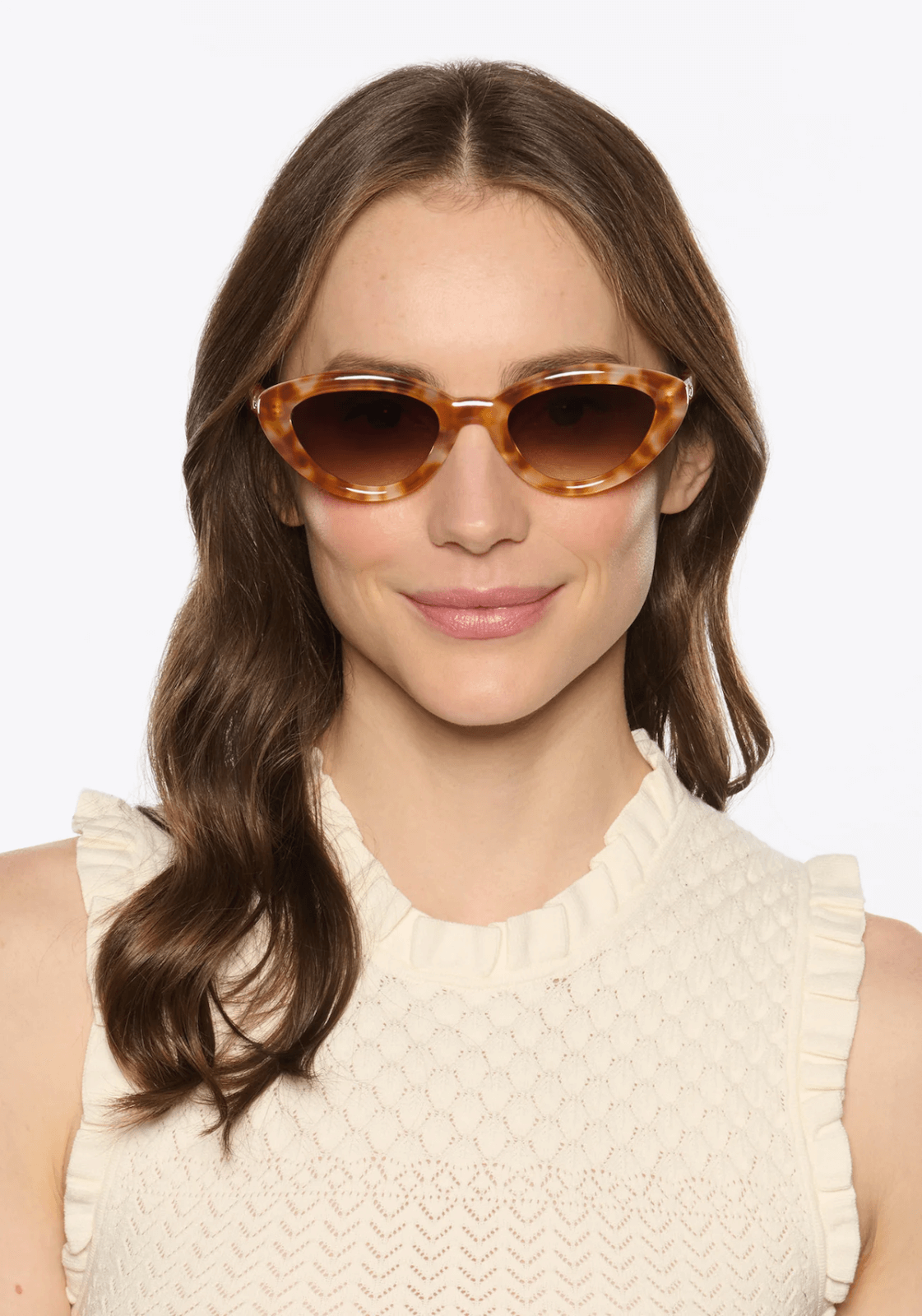Person with long hair wearing tortoiseshell sunglasses and a sleeveless, textured white top, smiling slightly at the camera, as if ready to explore the vibrant treasures of Nashville in March.