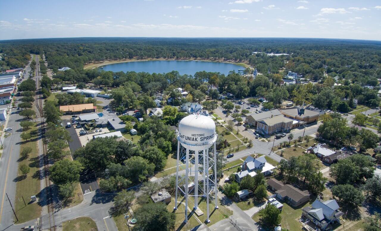 Aerial view of DeFuniak Springs with a water tower and lake in a small town setting.