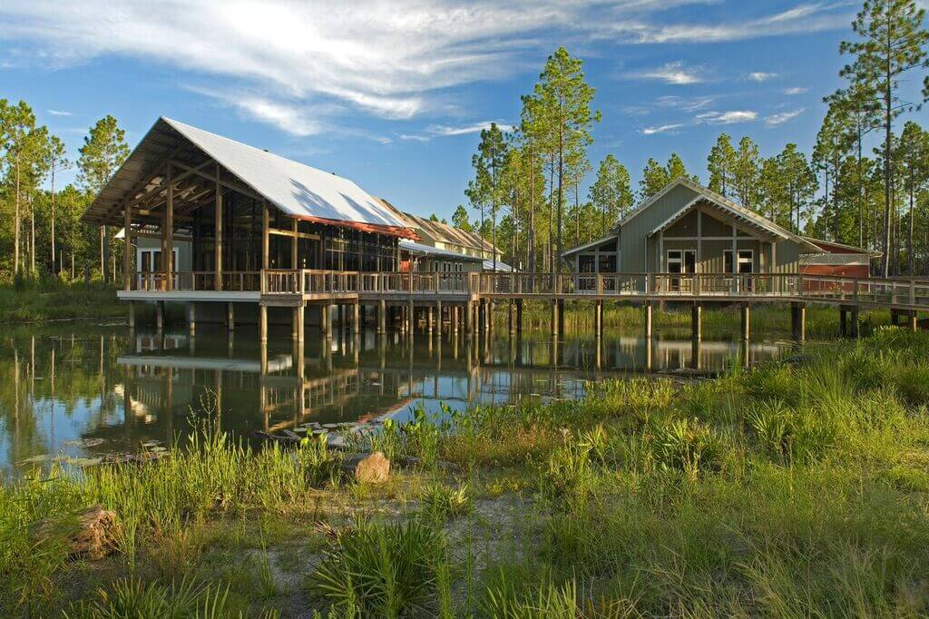 Stilted buildings with large verandas overlooking a tranquil pond surrounded by greenery.