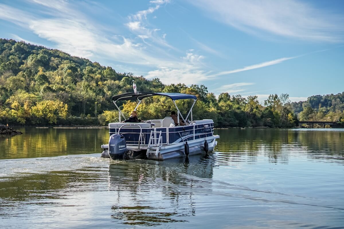 6 Southern Outdoor Getaways for the Adventure Traveler - 8 A pontoon boat cruising on a calm river with a backdrop of hills and a clear blue sky.