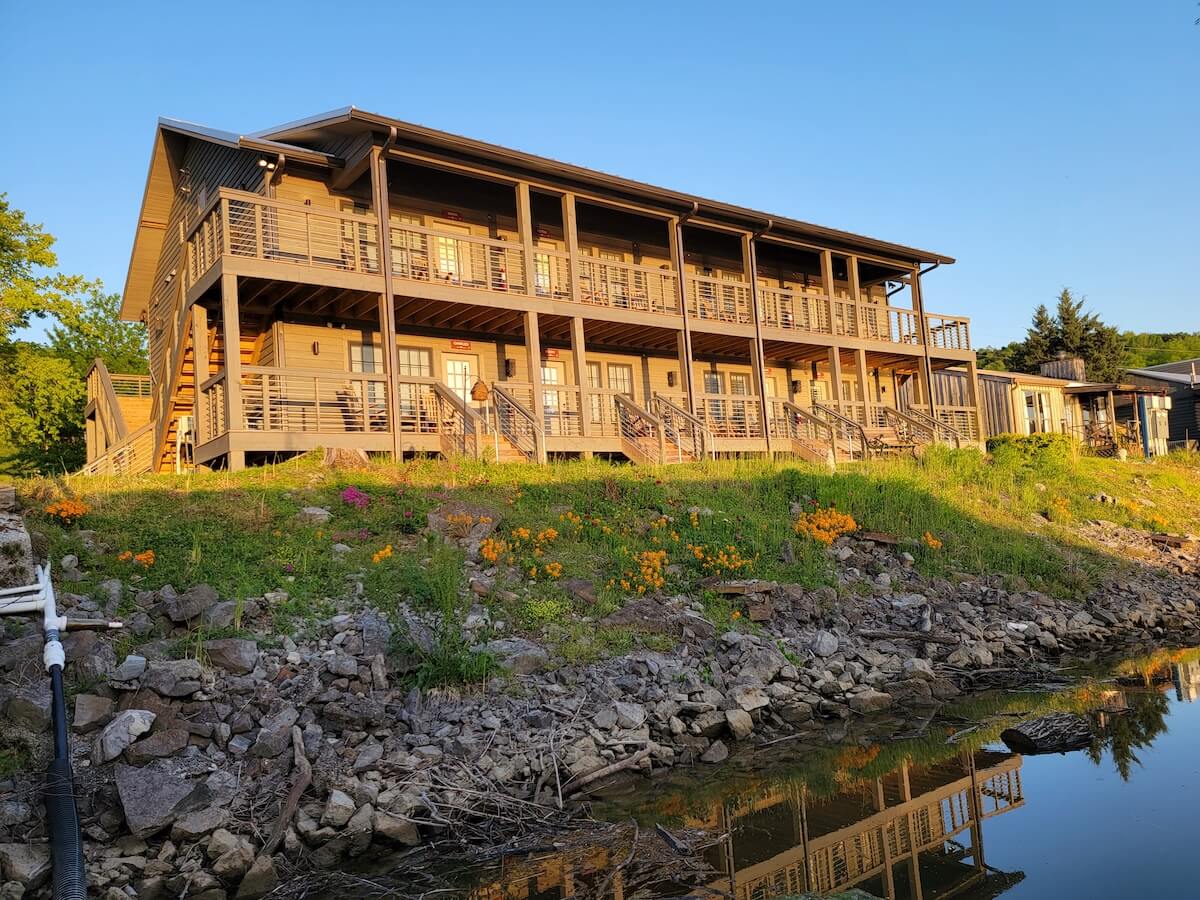 A multi-story wooden building with balconies overlooking a waterfront at sunset.