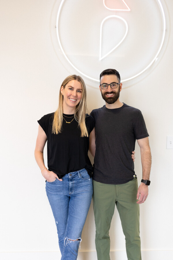 A man and woman standing in front of a neon "Hi Finch" sign.