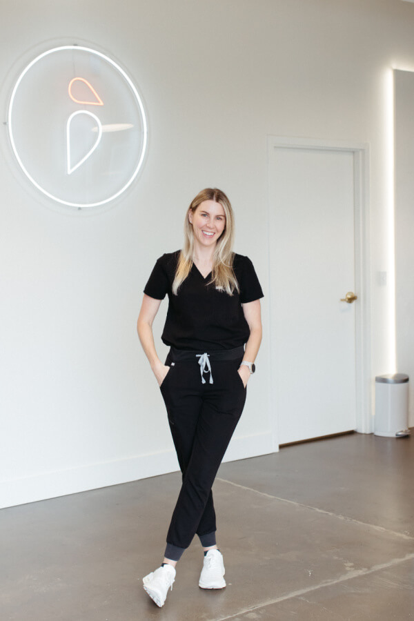 A woman in black standing in front of a neon sign.