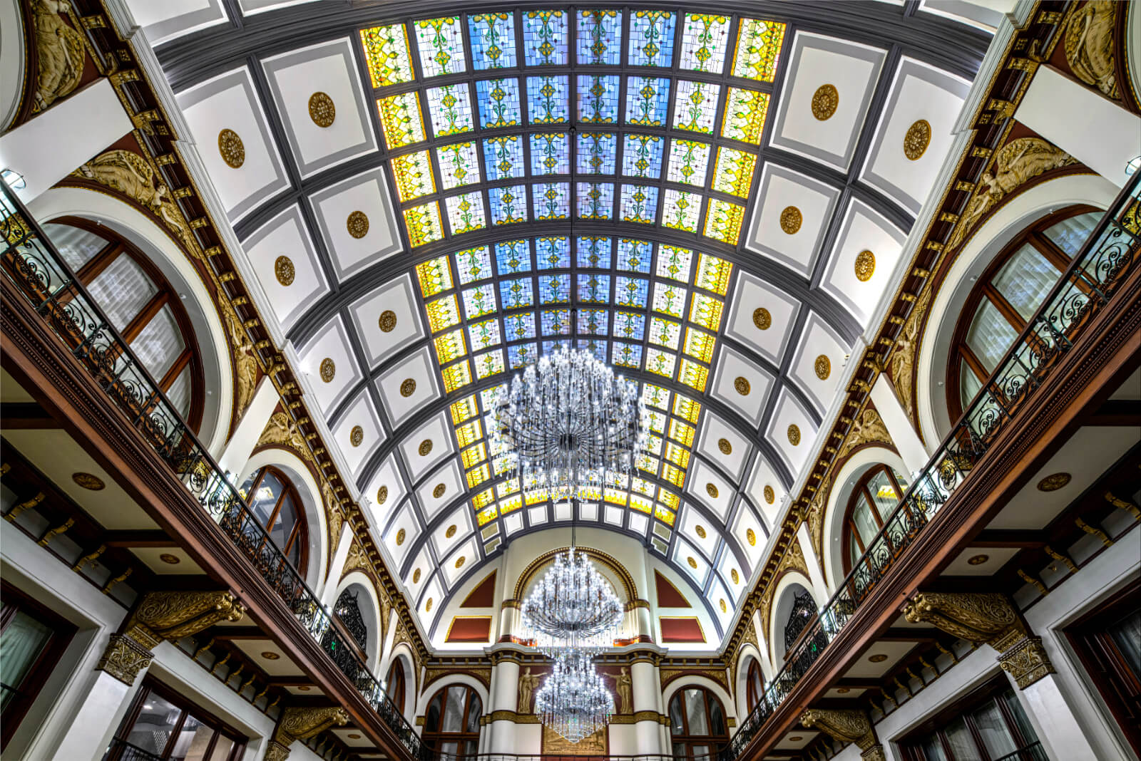 Elegant interior of a grand building featuring an arched ceiling with stained glass and a central chandelier.