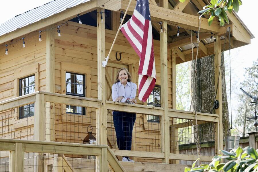 Keith Maddin standing on the balcony of a wooden treehouse with an American flag hanging nearby.