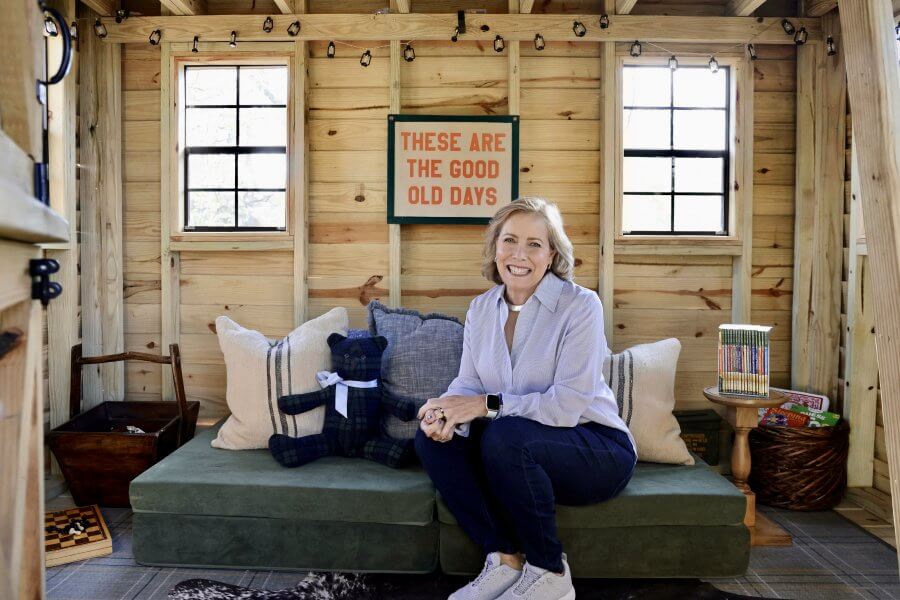Keith Maddin smiling in a cozy wooden cabin with a sign that reads "these are the good old days.