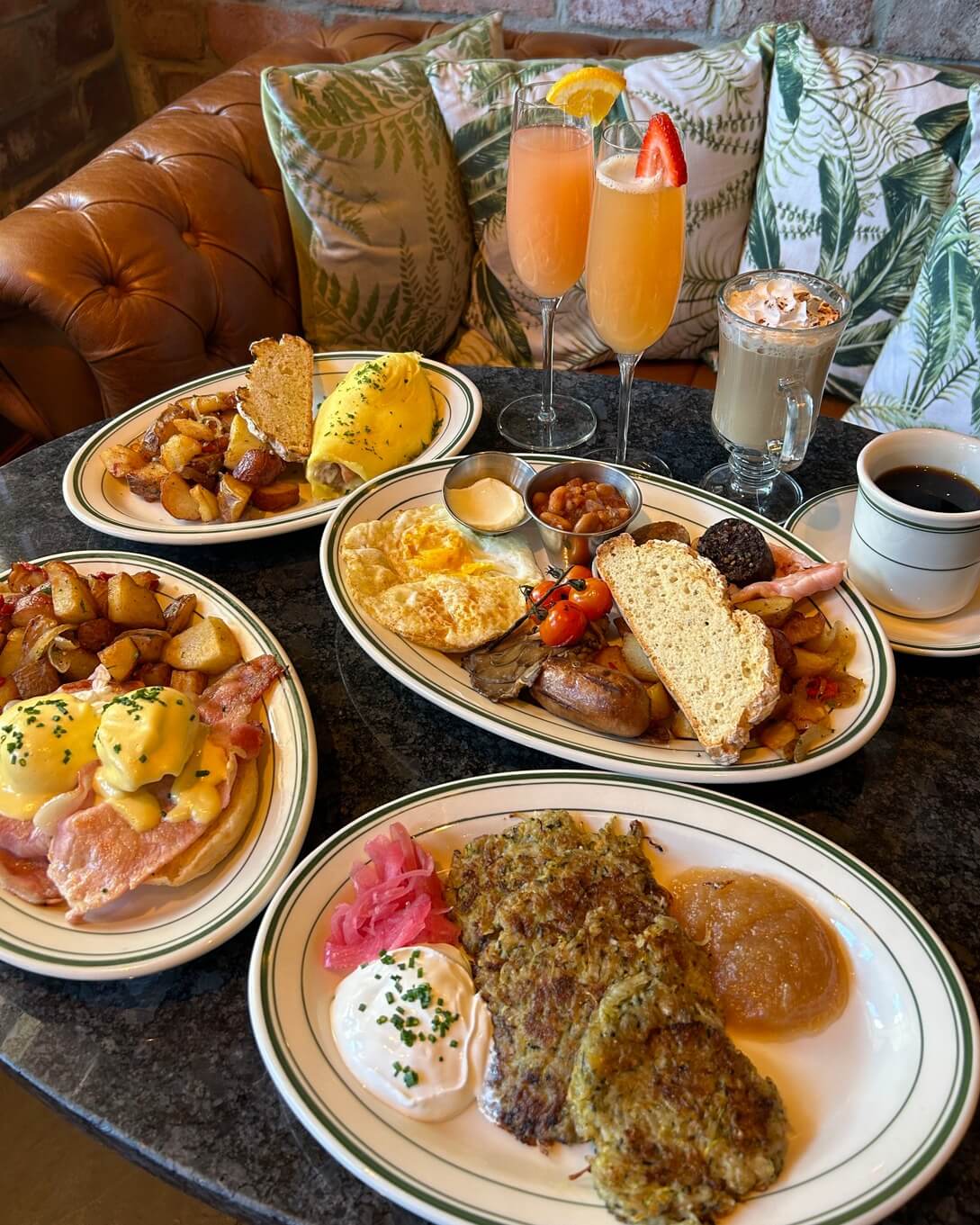 A brunch in Memphis features a table laden with breakfast delights like eggs Benedict, an omelette with potatoes, a full English breakfast, and hash browns with poached eggs, alongside beverages such as coffee and cocktails.