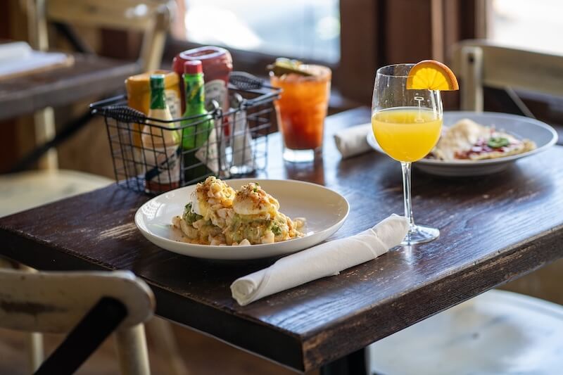 A plate of brunch delights sits next to a rolled napkin on a wooden table, accompanied by a drink garnished with an orange slice. Condiments and another drink hint at the vibrant dining scene in Memphis.