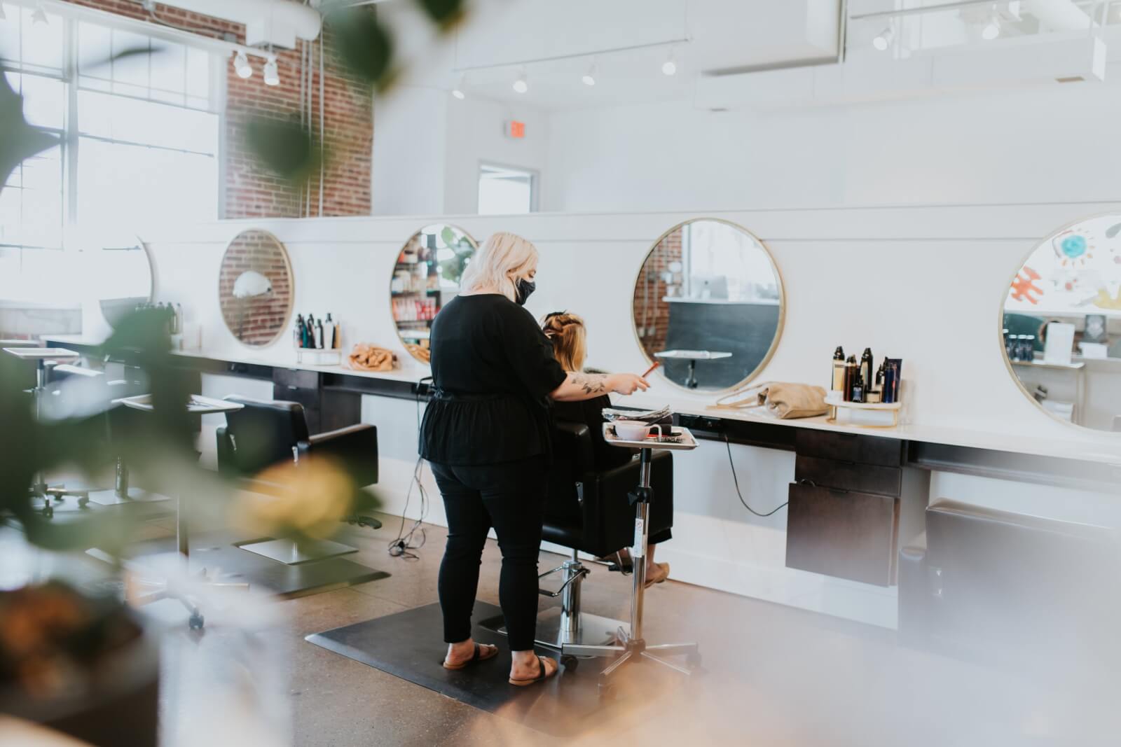 A hairstylist in a black outfit is expertly cutting a client's hair in one of the best hair salons, known for spa services, featuring modern touches like large round mirrors and sleek styling stations.