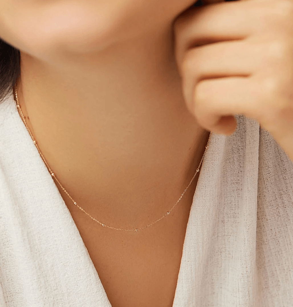 Close-up of a woman's neck wearing a delicate gold necklace, complemented by a white blouse.