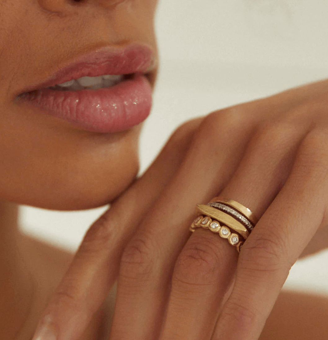 Close-up of a person's hand with three elegant rings, touching their lips