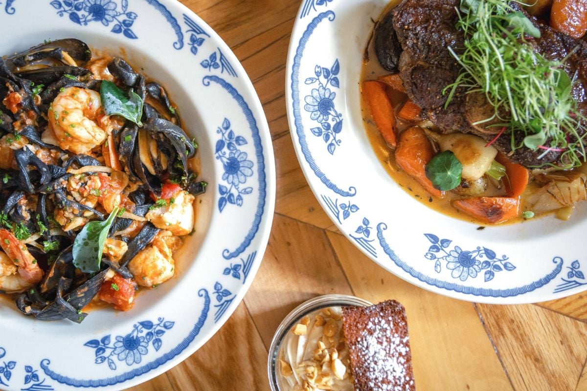 Two plates with shrimp pasta and braised meat with vegetables, plus a small dessert, served on a wooden table in the heart of Germantown Louisville.