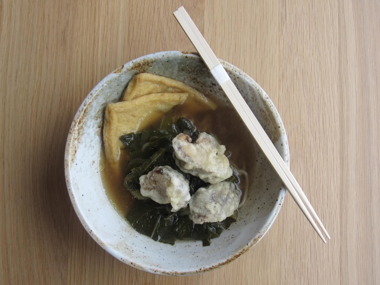 A bowl of asian soup with tofu, seaweed, and oyster tempura, served with a pair of chopsticks on a wooden table.